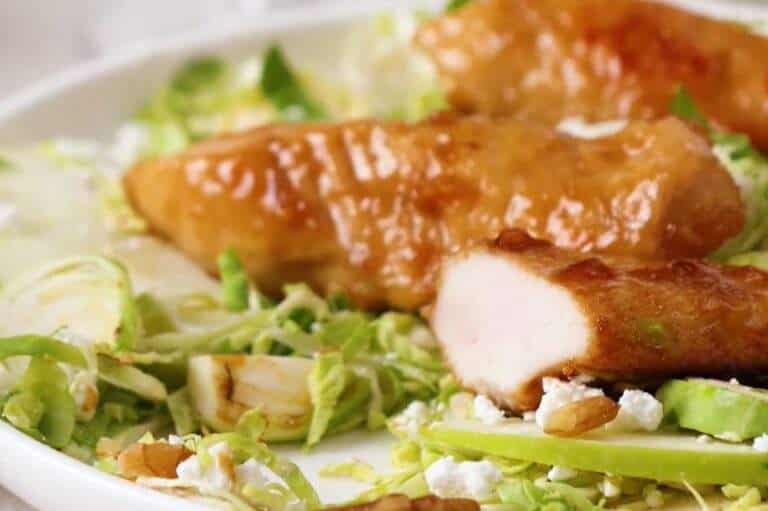 Apple and Honey-Glazed Chicken Tenders Recipe served on a plate with shredded greens, apple slices, goat cheese, and toasted nuts, showcasing a golden glaze and tender chicken texture.