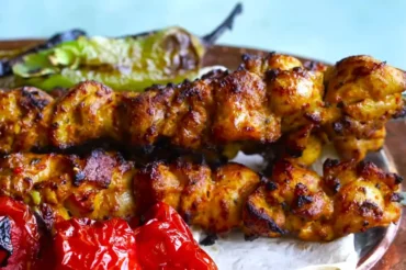 Grilled Shish Tawook skewers with a golden, crispy exterior, served with roasted tomatoes and green peppers on a traditional Middle Eastern platter. Juicy and flavorful marinated chicken kebabs, a popular dish in Mediterranean and Middle Eastern cuisine.