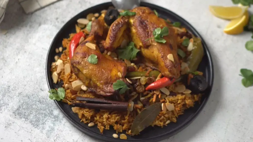 Authentic Chicken Kabsa dish featuring spiced roasted chicken over aromatic basmati rice garnished with almonds raisins chili peppers and fresh herbs