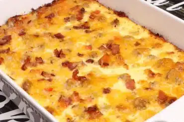 Freshly baked Sausage And Egg Casserole With Crescent Rolls in a white baking dish, topped with crispy bacon, melted cheddar cheese, and golden-brown edges. A hearty and delicious breakfast casserole perfect for brunch or meal prep.