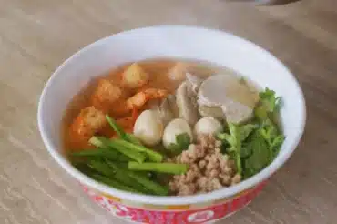 House Special Soup served in a white bowl with shrimp, quail eggs, sliced pork, minced meat, fresh greens, and a flavorful broth. A hearty and delicious dish.