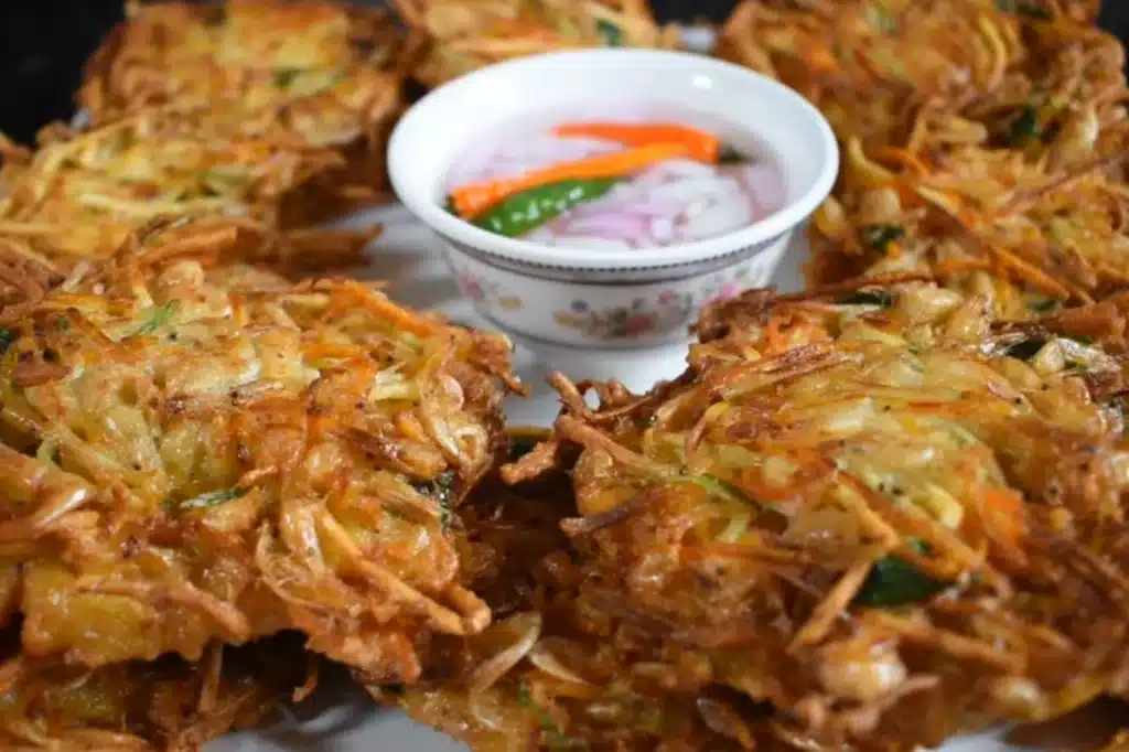 Crispy sweet potato ukoy fritters with palabok noodles, garnished with onions and peppers – Filipino fusion delight