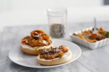 Bagels topped with creamy spread and carrot lox from Simple Carrot Lox Recipe Washington Post Recipe served on a white plate with seasoning in background.