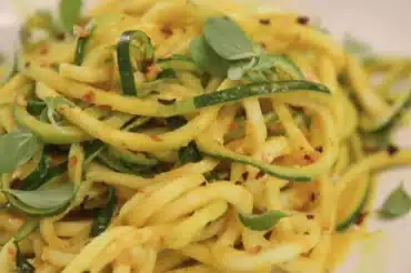 Close-up of zucchini noodles almondine garnished with fresh herbs and red pepper flakes, showcasing the best noodles almondine recipe