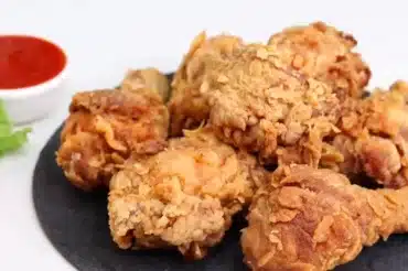 Crispy golden fried chicken pieces on a black plate with a side of red dipping sauce and fresh lettuce. Is Chicken Tenders a Food Analog Find out here