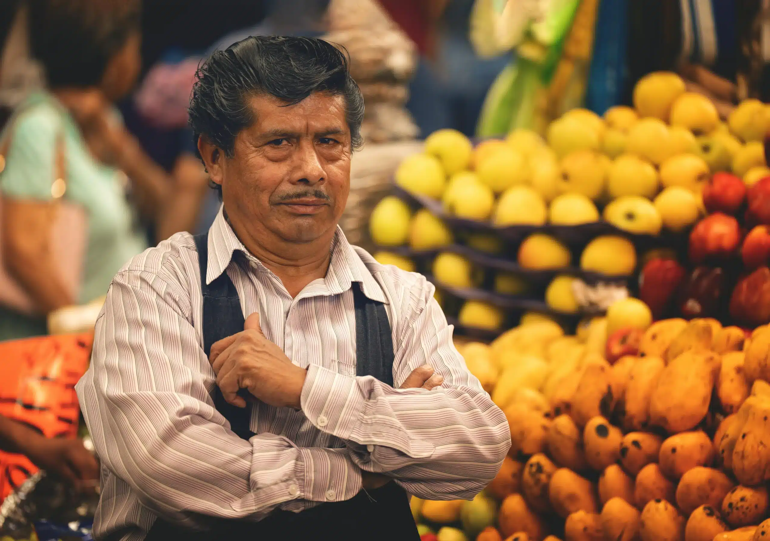 A man tending to his stall in a colorful Mexican market, with piles of fresh produce.