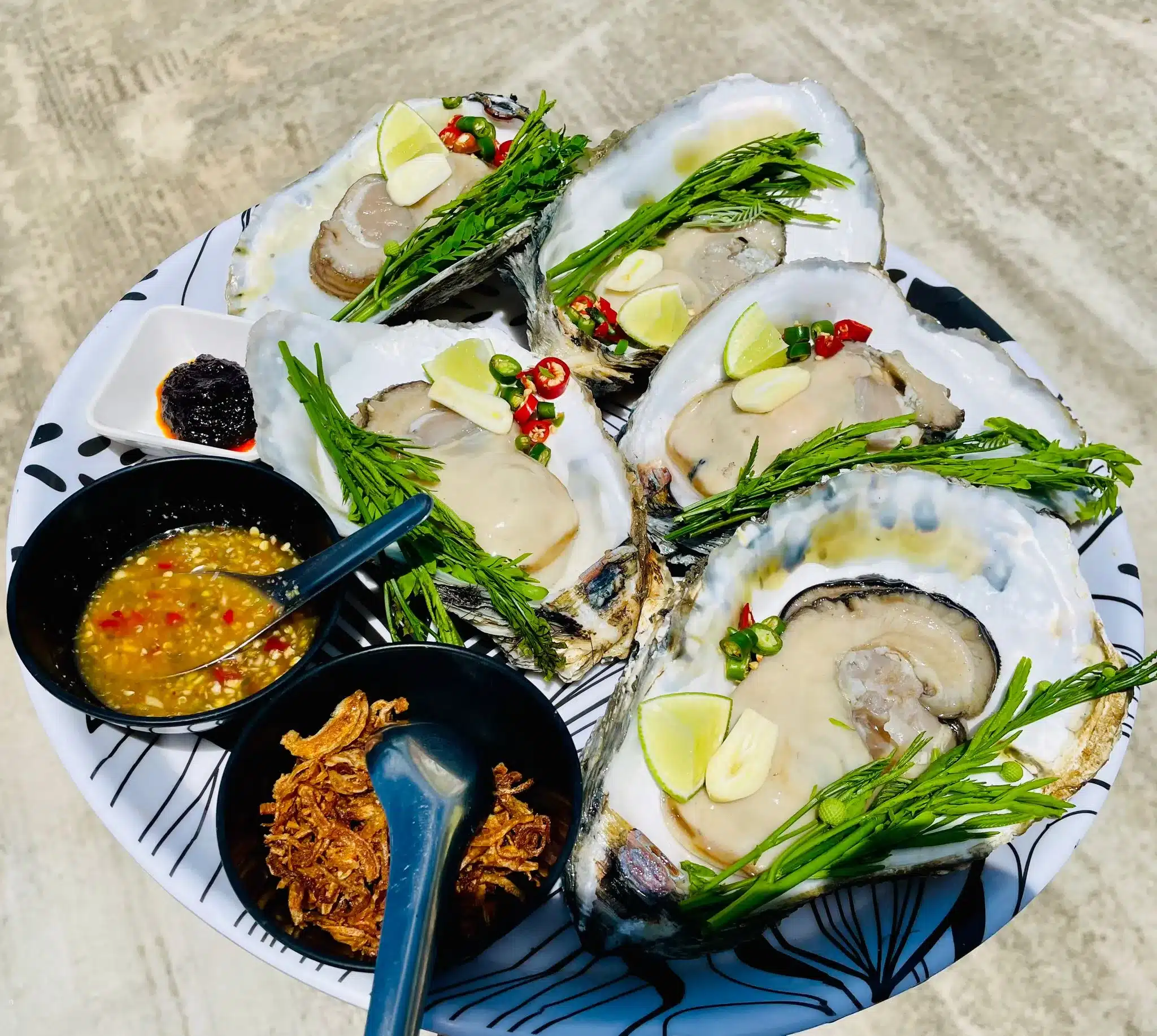 A platter of fresh oysters served with traditional Thai condiments like fried shallots, chili, garlic, and fresh herbs.