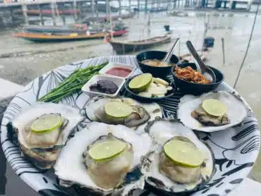 Oysters on the table with traditional sides, with fishing boat behind