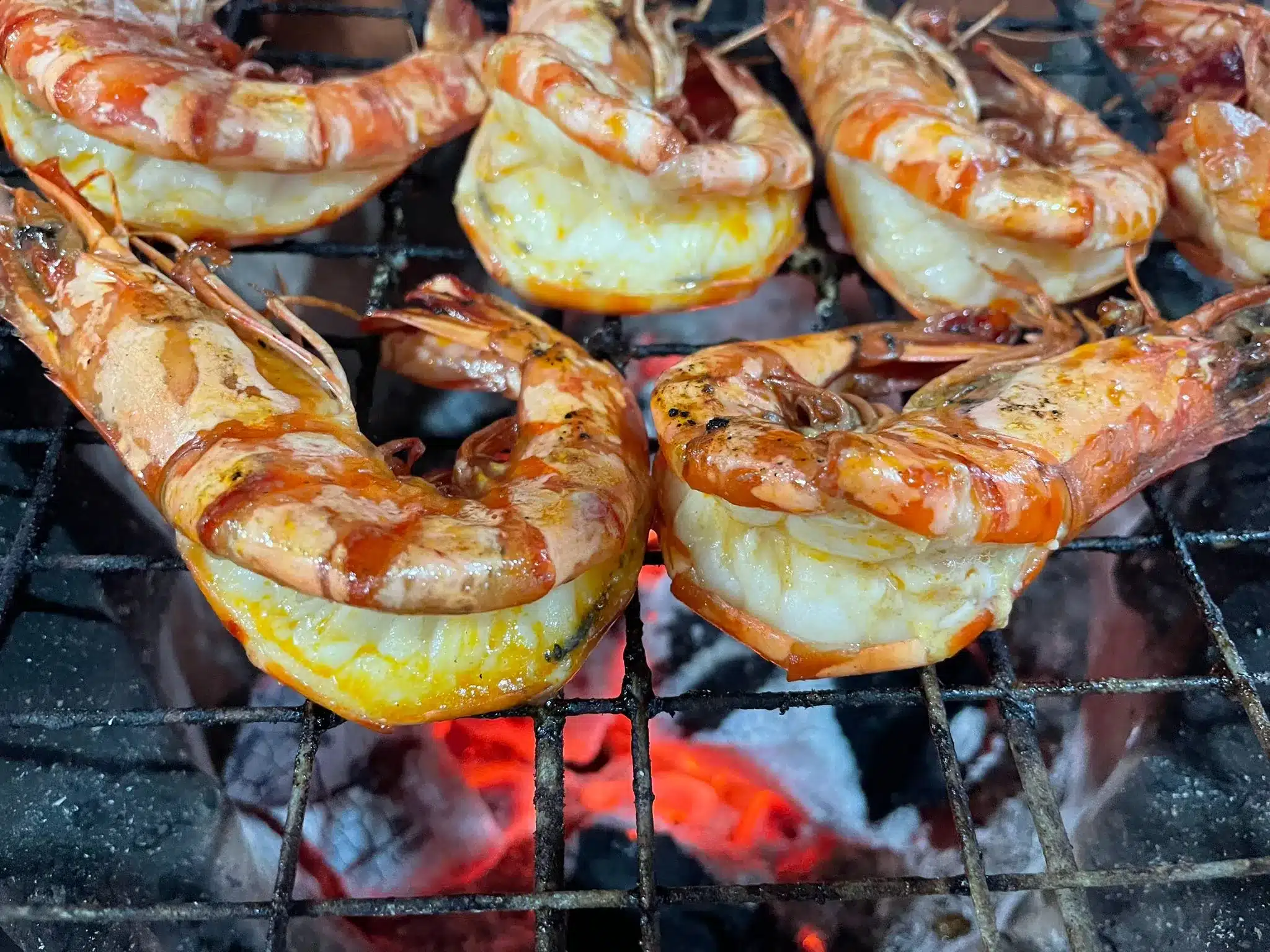 Large prawns cooking on a charcoal BBQ, split down the back.