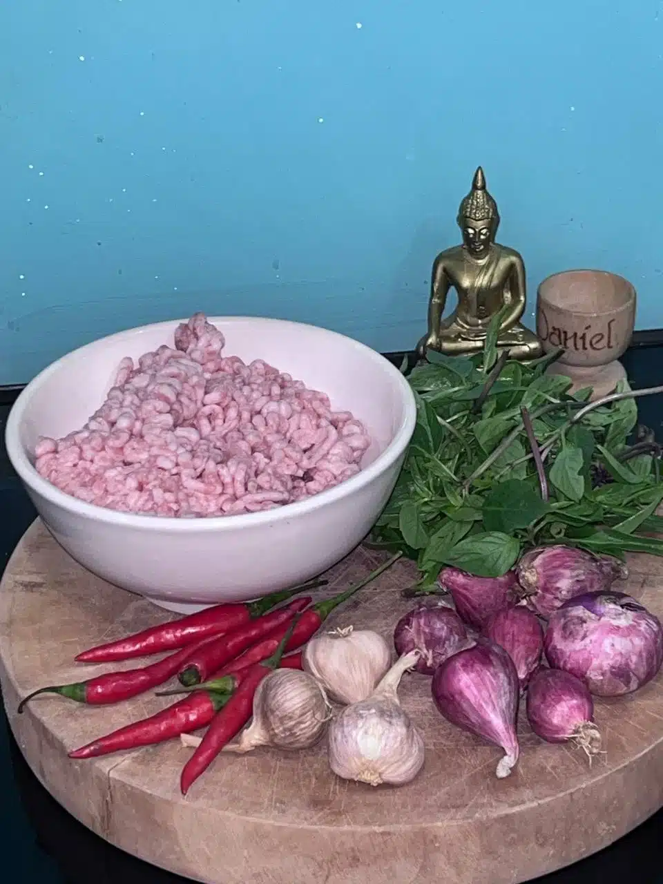 Raw ingredients for Pad Kra Pao with a small Buddha and wooden egg pot inscribed with ‘Daniel’