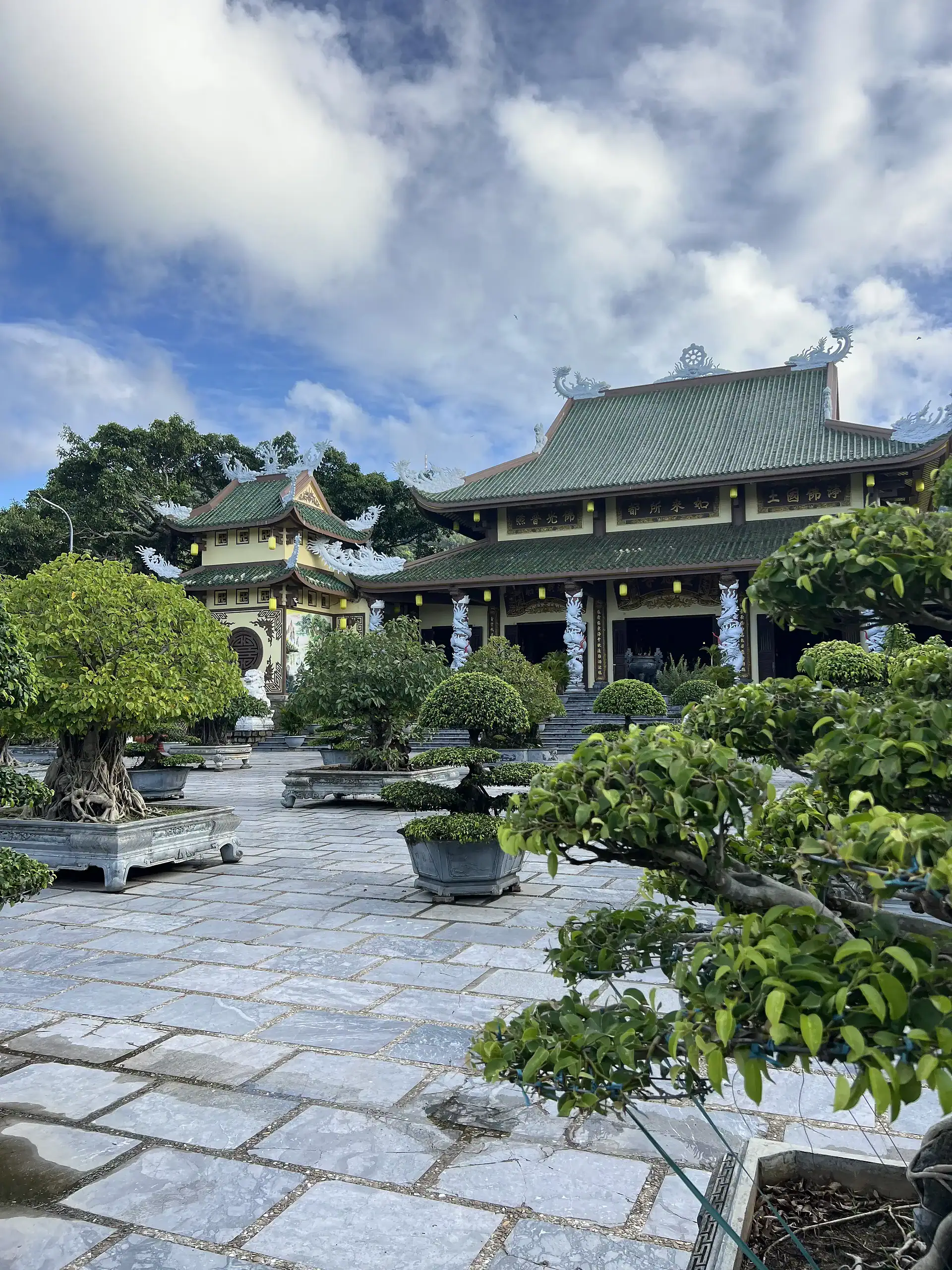 Discover Da Nang in 2025: The Most Comprehensive Travel Guide to Vietnam’s Coastal Gem 6 Green traditional Asian temple surrounded by potted bonsai trees under cloudy sky.