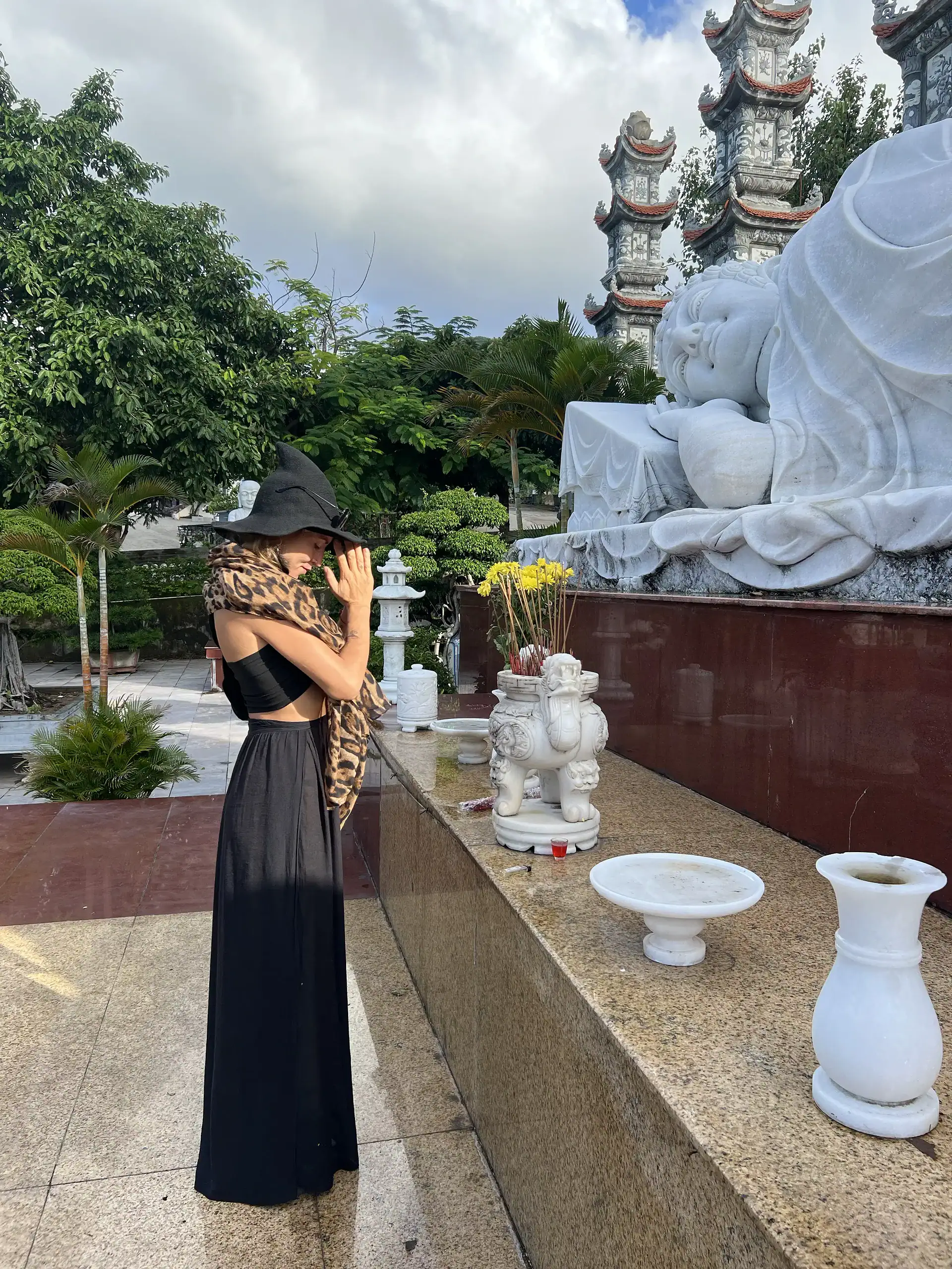 Discover Da Nang in 2025: The Most Comprehensive Travel Guide to Vietnam’s Coastal Gem 5 Intriguing woman in black dress and hat at a traditional Asian temple with marble statues and lush greenery.