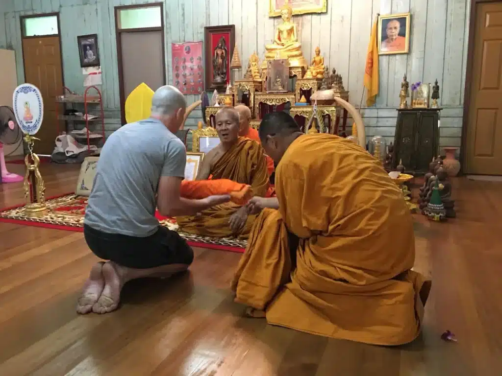 Oliver kneeling before head monk during monastic ordination ceremony on Koh Chang—Thai Buddhist tradition honoring brother's passing