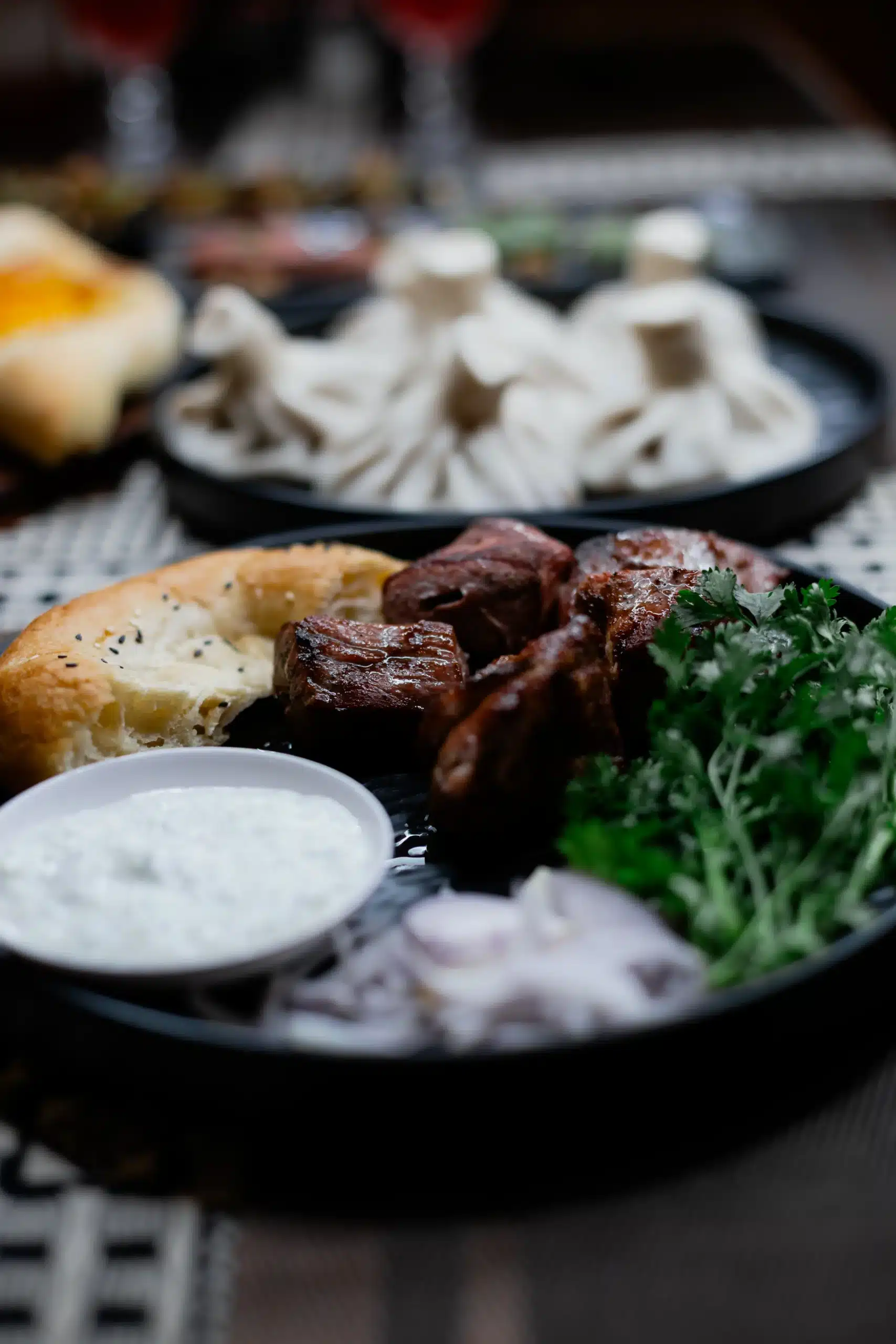 Charcoal-grilled pork shashlik served with fresh herbs and Khinkali dumplings in the background at Hinkali House Hua Hin, demonstrating the thermal respect protocol for Mangoes and Palm Trees.