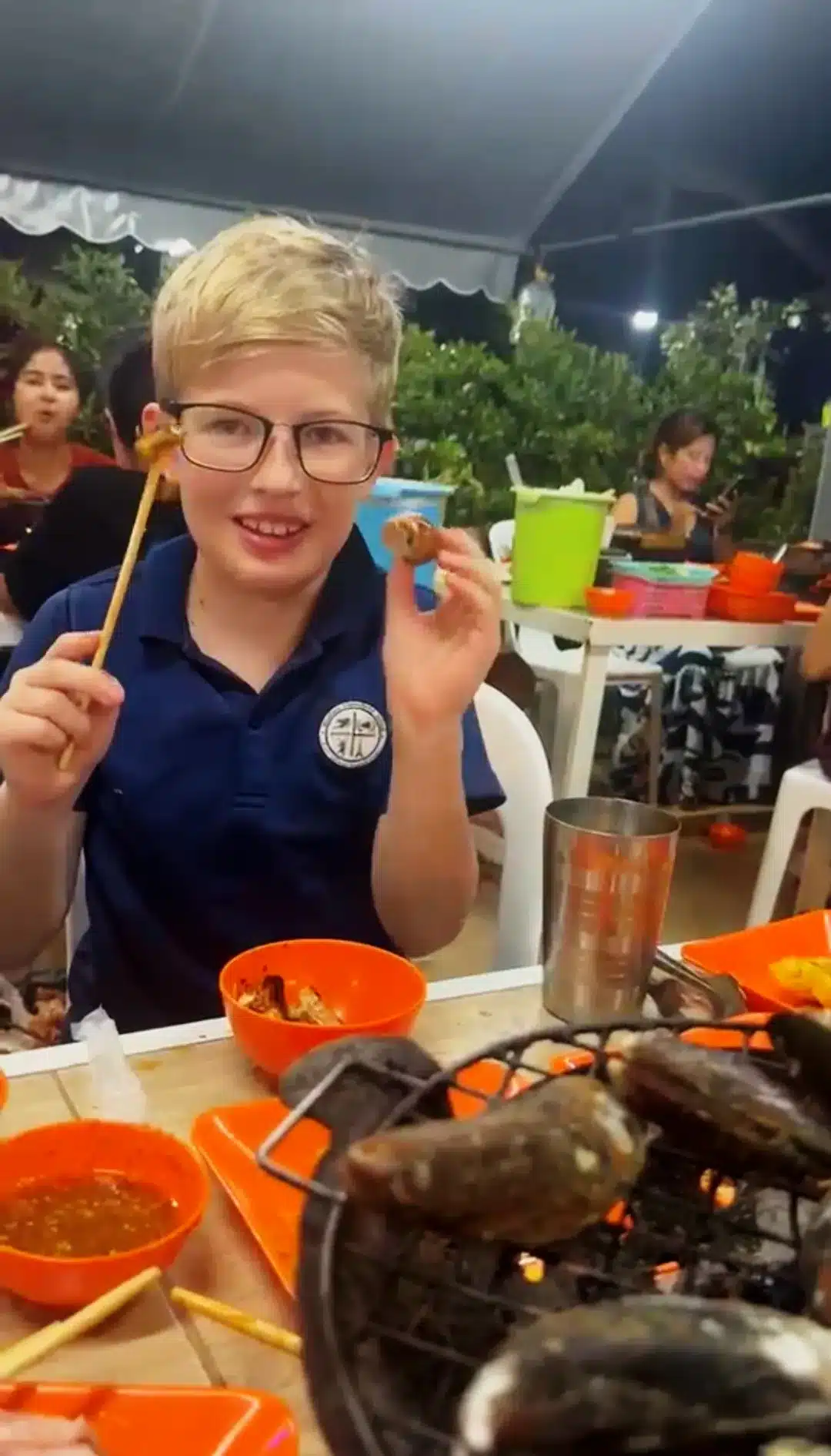 Victor holding a grilled mussel with chopsticks—first sea snail taste, July 2026 Koh Samui