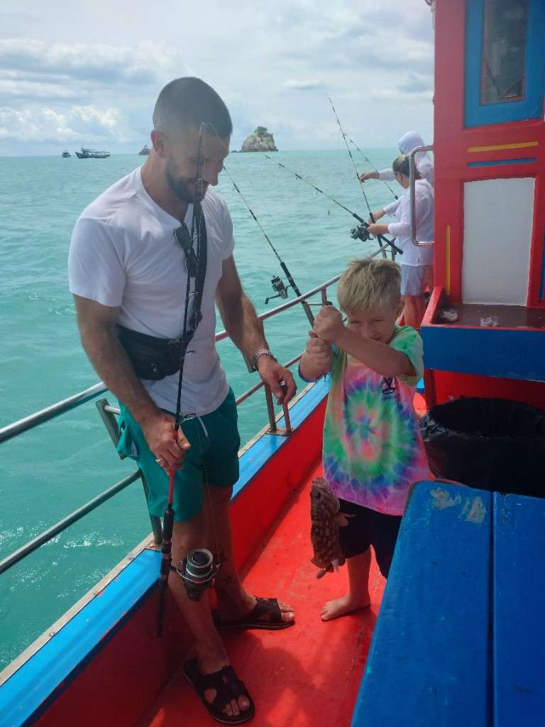 Victor smiles with a fresh catch while Oliver holds the rod on a Koh Samui deep-sea fishing trip