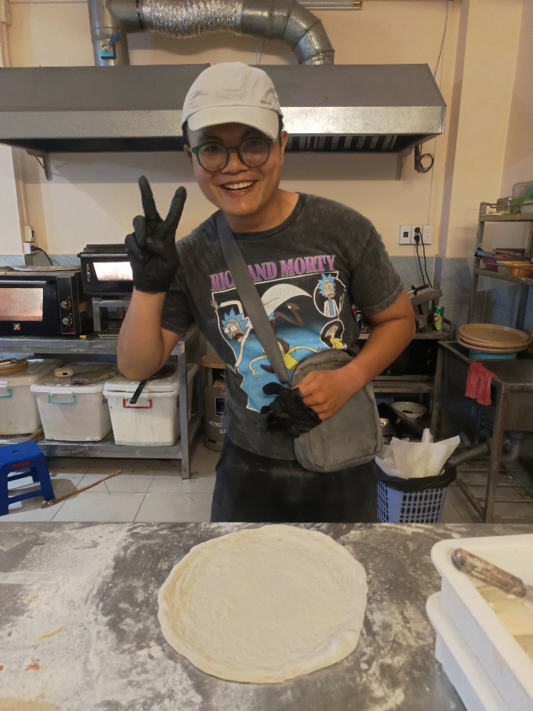 Bob, the owner of Pizza 100, in the kitchen with stretched pizza dough on a floured counter in Bình Thạnh