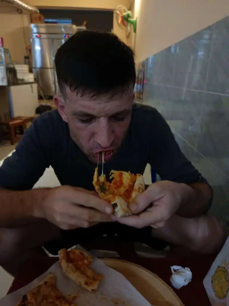 Oliver eating a slice of Pizza 100 pizza with melted cheese stretching from the slice