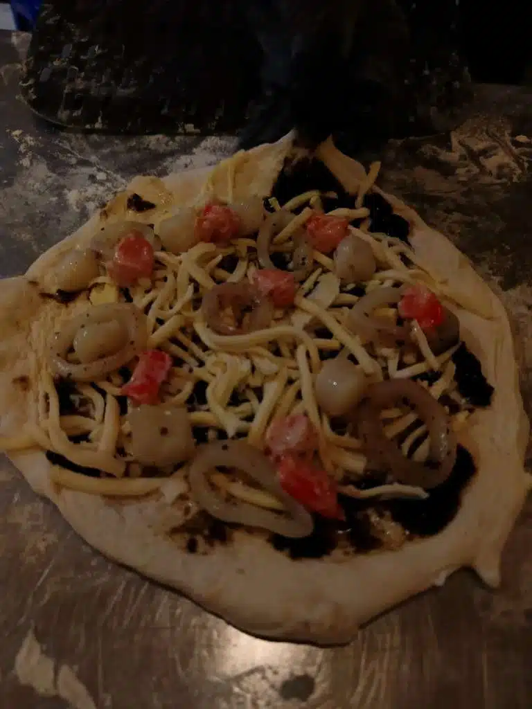 Unbaked pizza topped with seafood, onion, cheese, tomato, and black olives at Pizza 100
